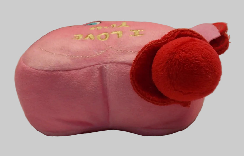 A pink plush pillow designed to look like a perfume bottle, featuring yellow embroidered text that reads 'I LOVE YOU' and a red plush pom-pom accent on the side, set against a wrinkled white fabric background.